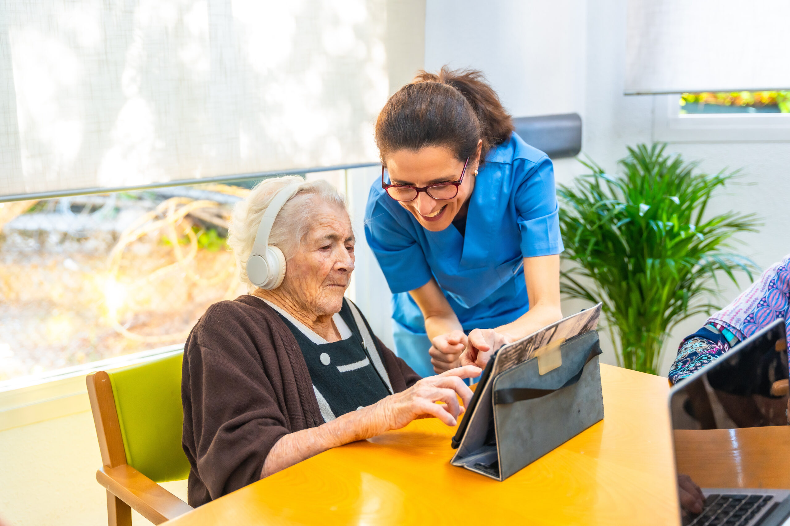 Senior woman and nurse using digital tablet and headphone in the geriatrics